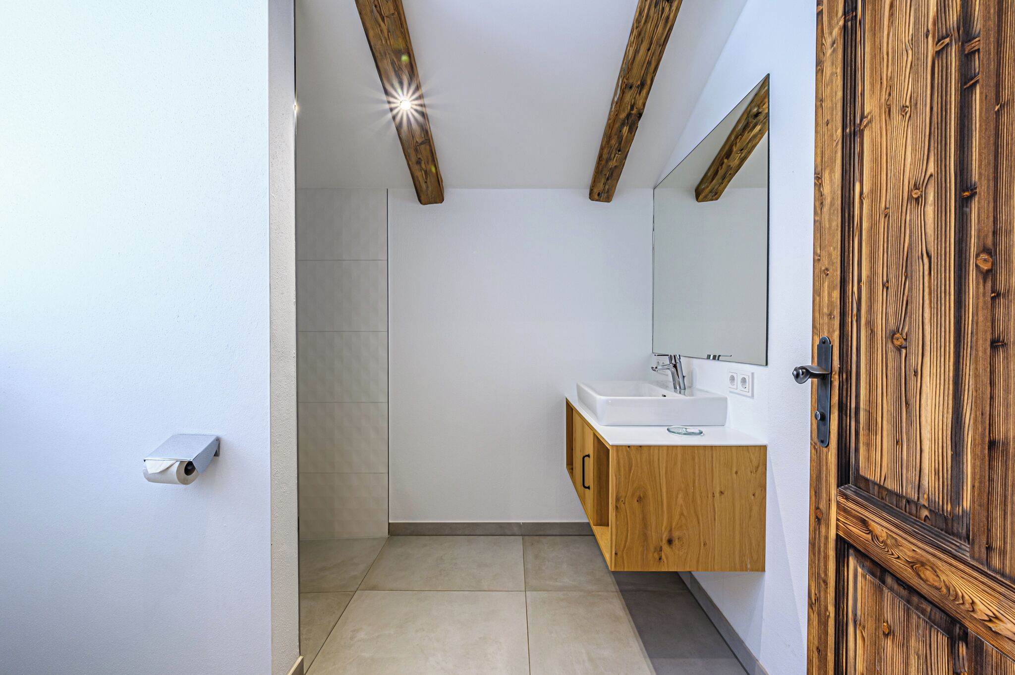 A modern bathroom with a wooden vanity, a large mirror, and a security camera.
