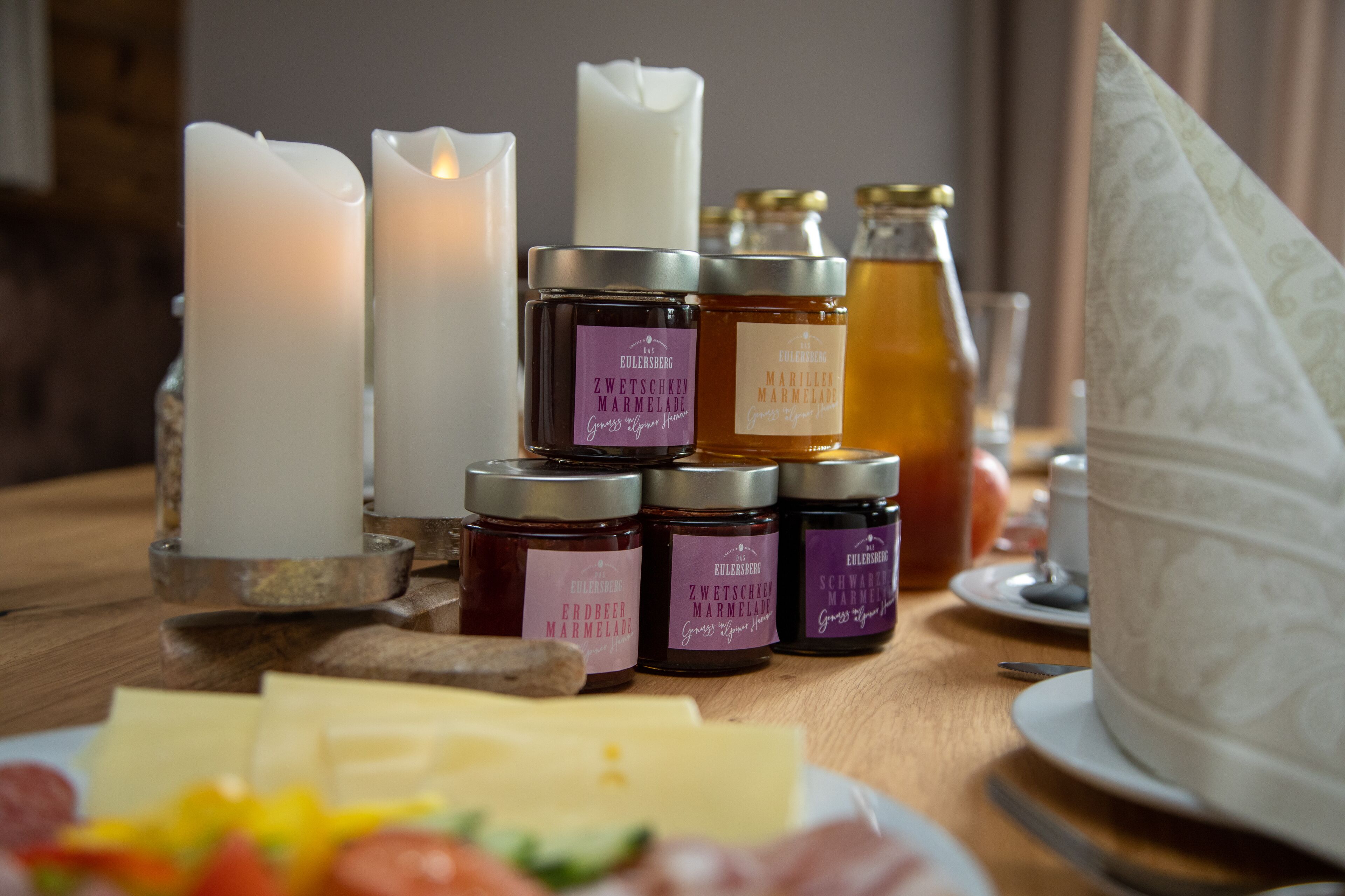 A table with candles, honey jars, cheese, and a white plate.