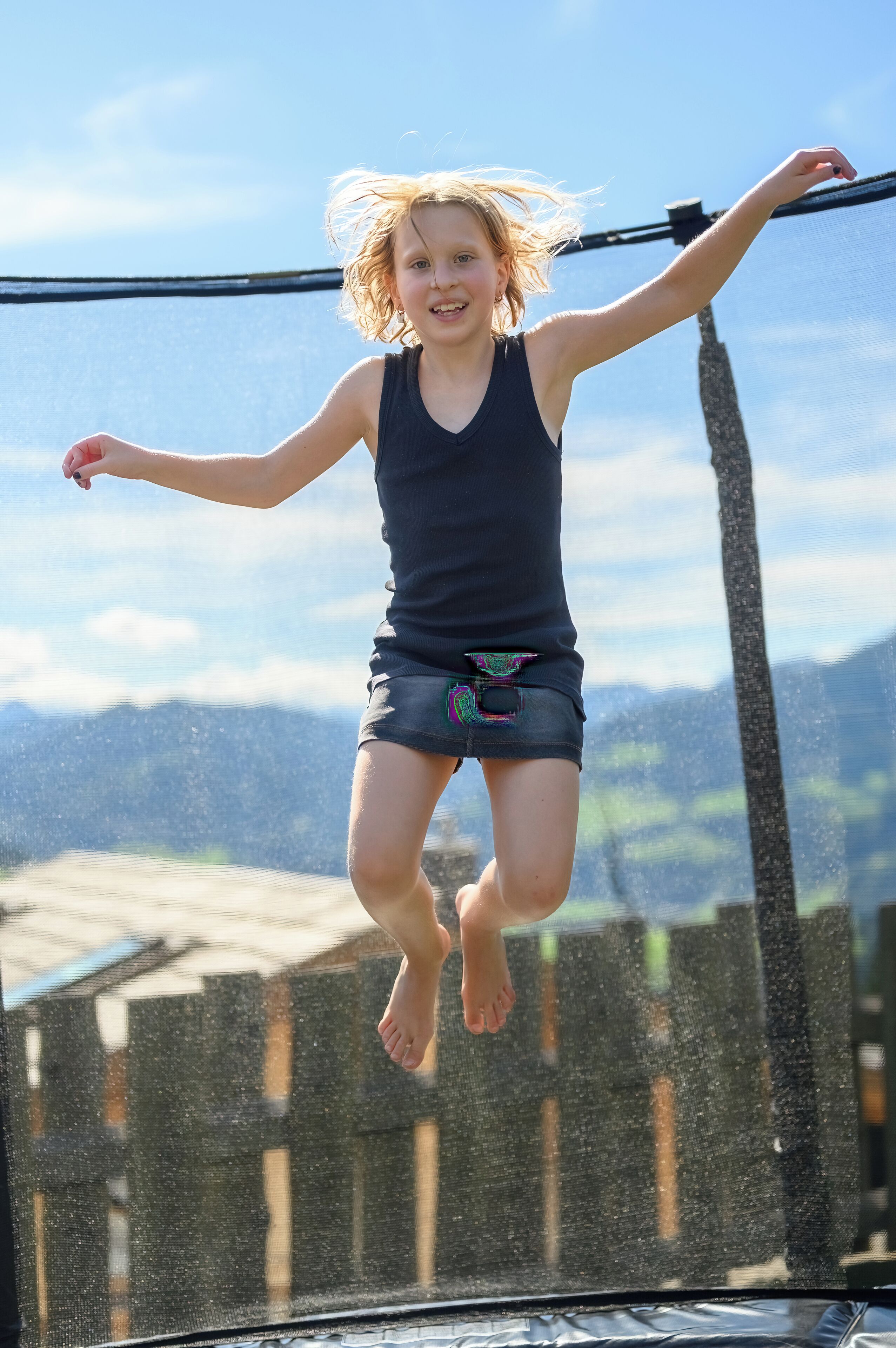 Una persona salta en un trampolín con vista despejada a una valla de madera y montañas al fondo.