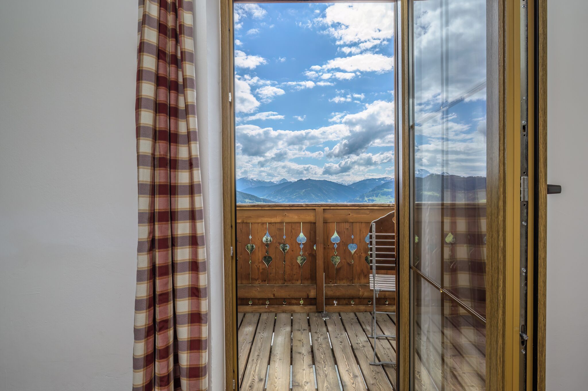 Een houten balkon met uitzicht op bergen en een bewolkte lucht.