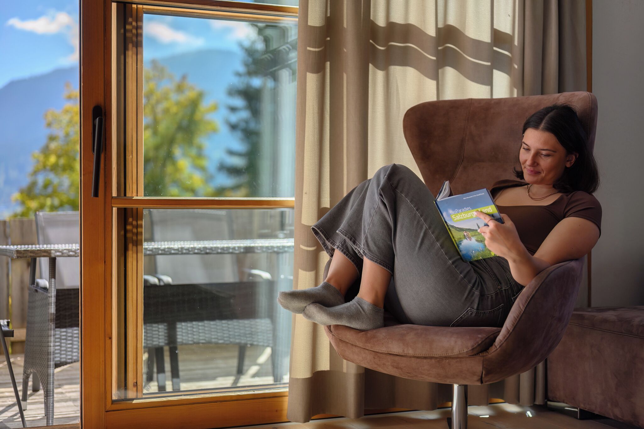 A person sitting in a chair by a window with a view of trees and mountains.