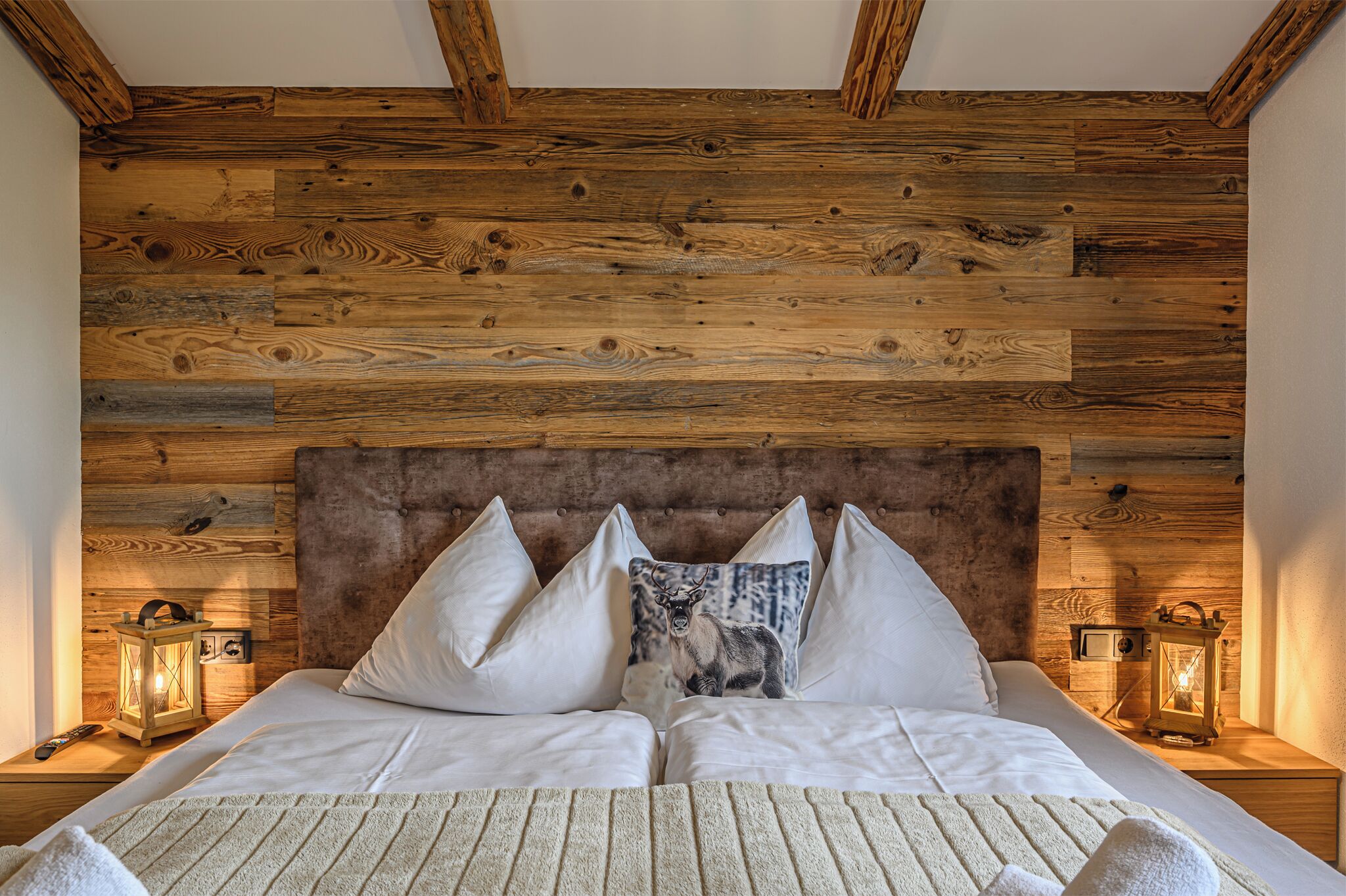 A bed with white linens, two pillows, a decorative pillow with a deer image, and two wall-mounted lanterns.