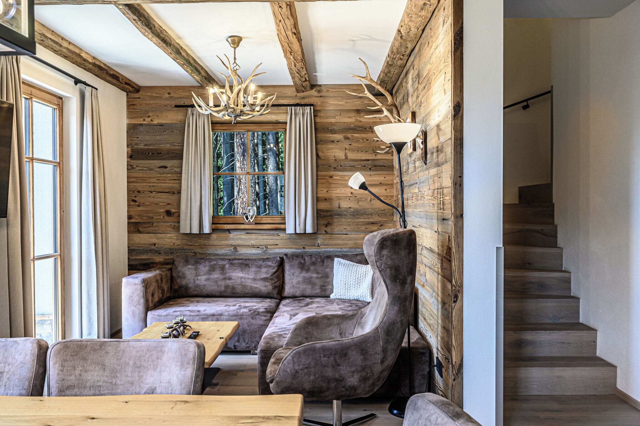 A rustic interior with a wooden wall, a sofa, a chandelier, and a staircase.