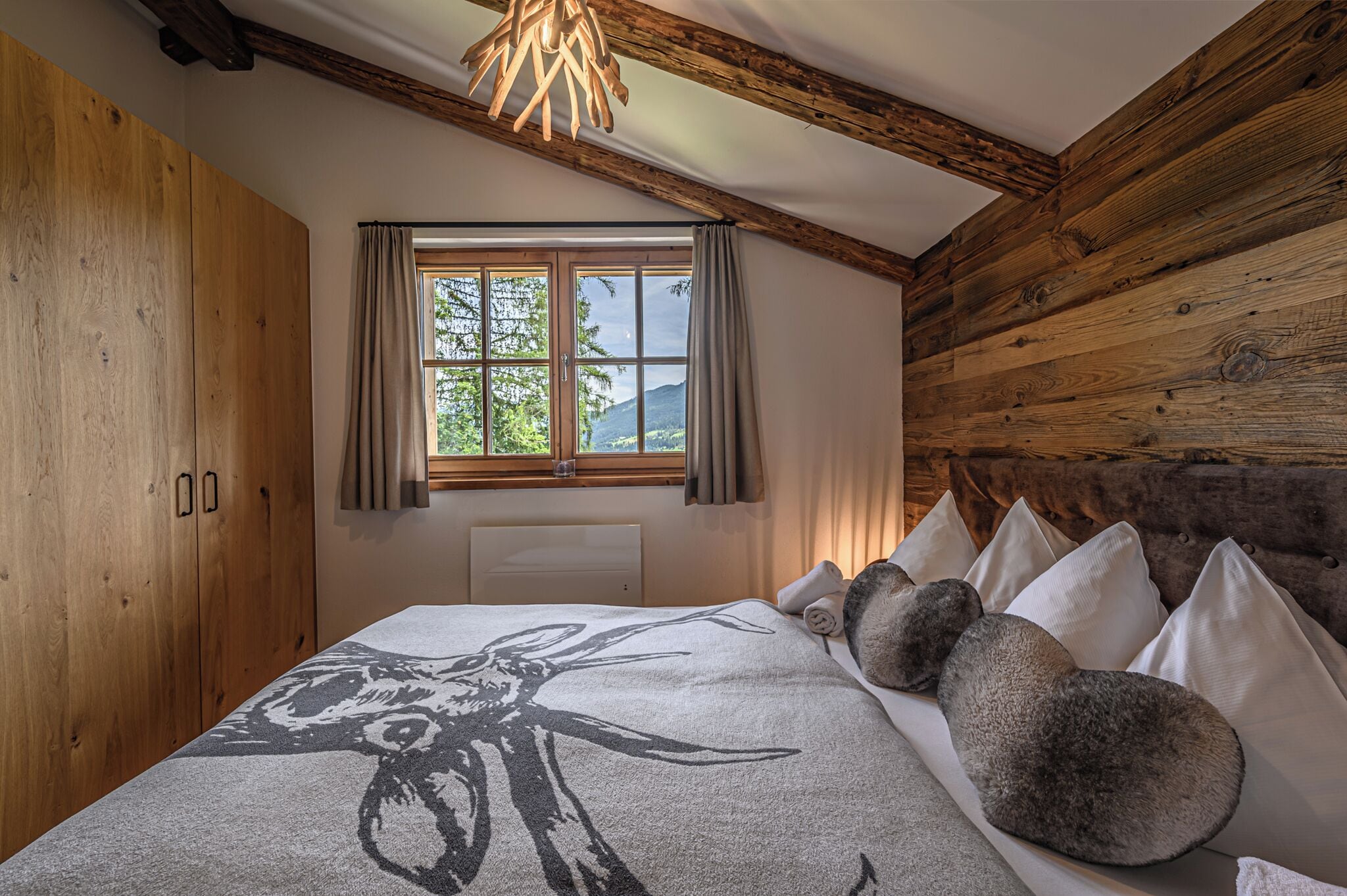 Une chambre avec un plafond en bois, un grand lit recouvert d’une couverture à motifs et une fenêtre avec des rideaux.