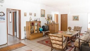 Un salón amplio con una mesa de comedor de madera, un sofá y una televisión. Hay varias fotos enmarcadas en las paredes y un globo terráqueo sobre la mesa.
