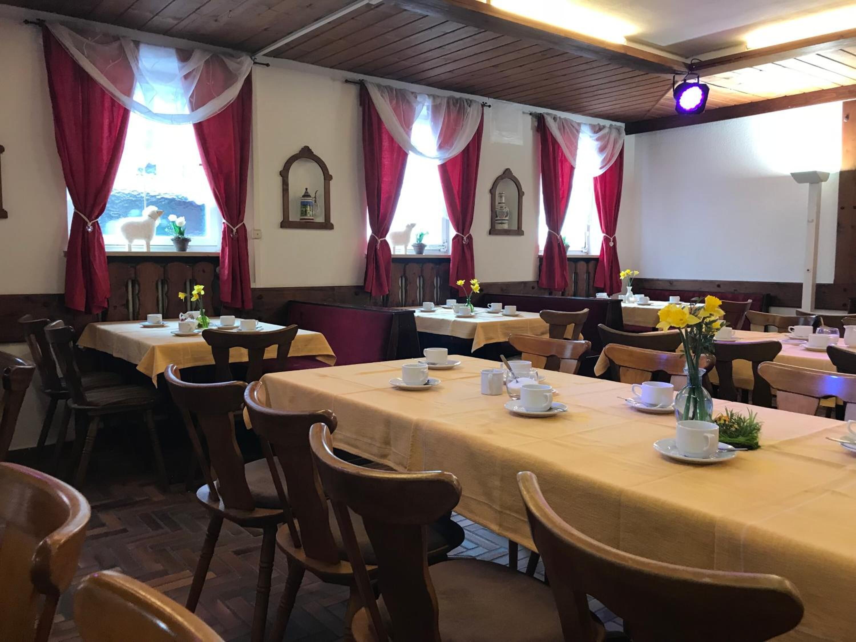 Ein Essbereich mit gedeckten Tischen für Tee, mit weißen Teetassen und Untertassen sowie floralen Mittelpunkten.