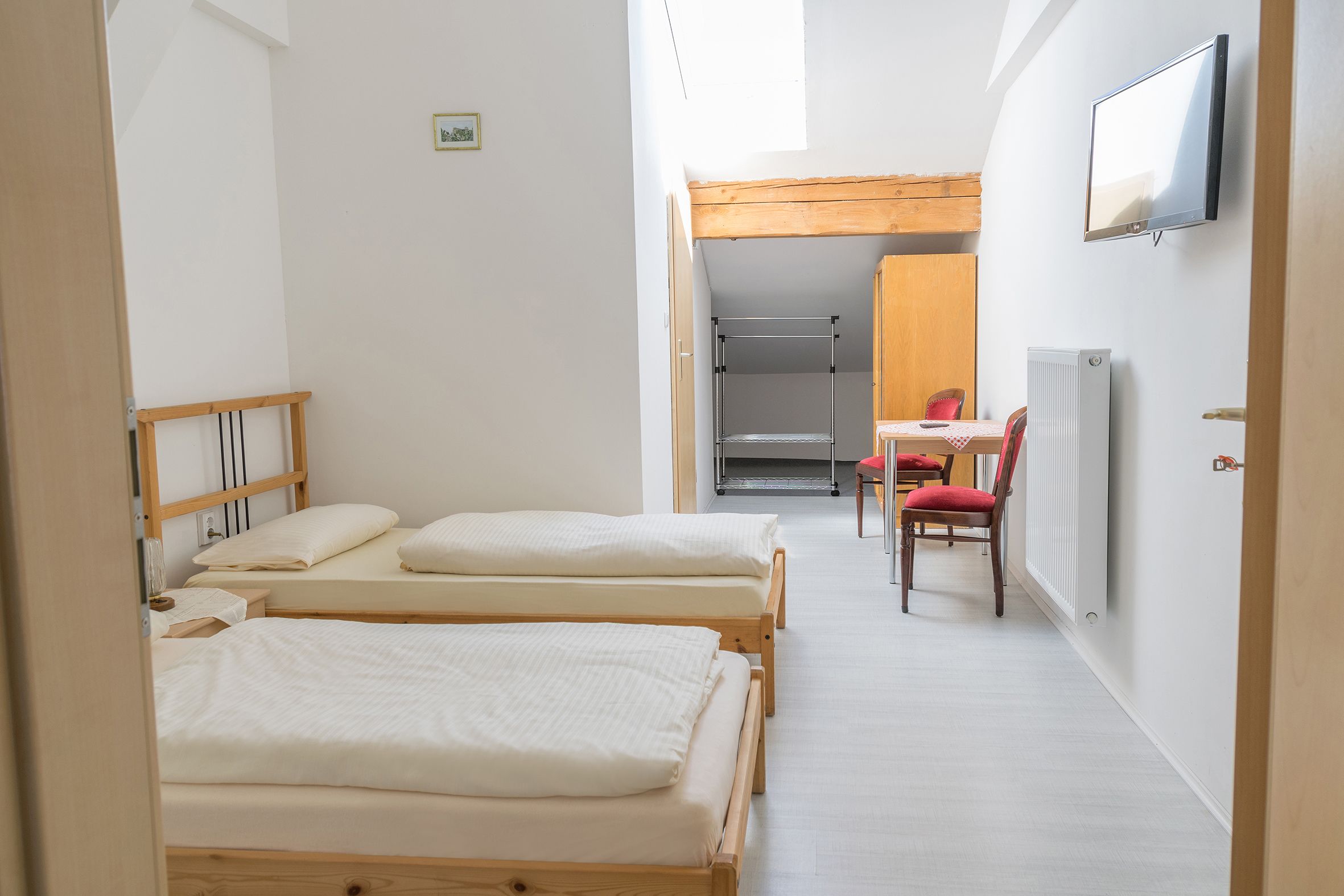 Een studentenkamer met drie eenpersoonsbedden, een bureau met stoel, een radiator en een aan de muur bevestigde televisie.