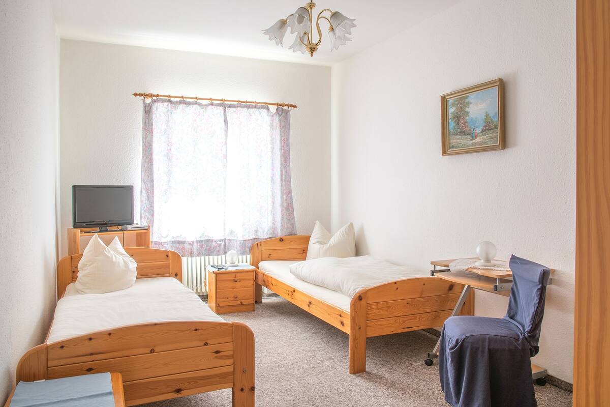 Un dormitorio con dos camas de madera, un escritorio con silla, un televisor y una ventana con cortinas.
