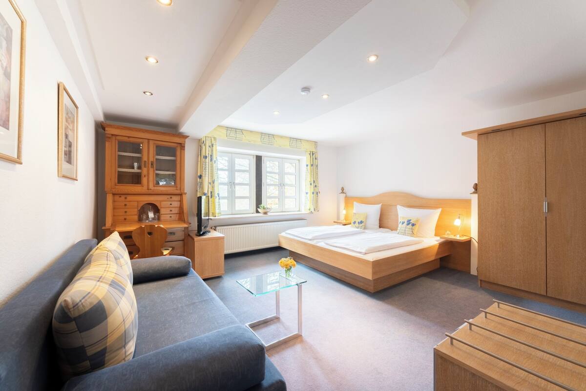 Quarto de hotel moderno com cama, sofá, armário de madeira e uma pequena mesa com flores.