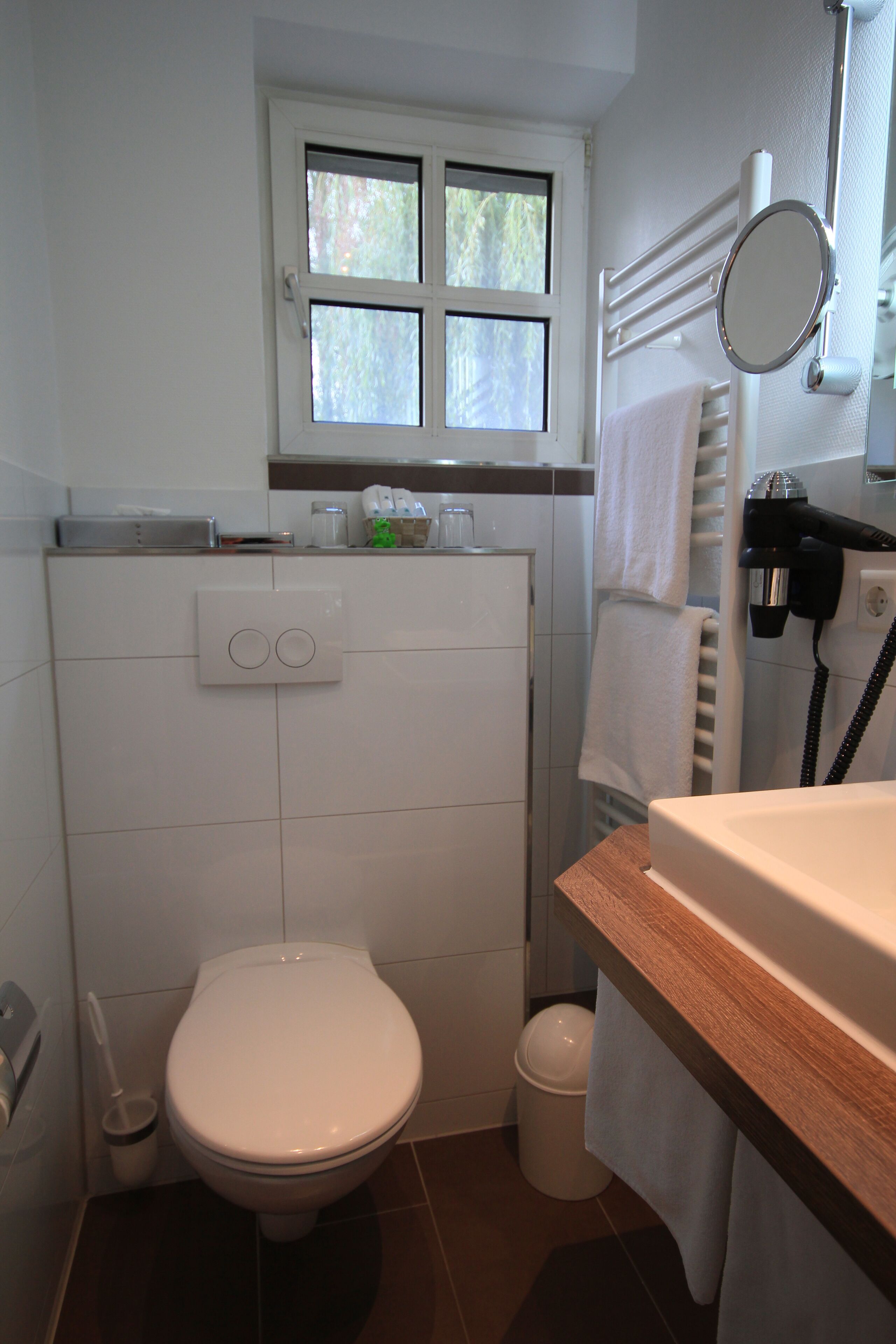 Un baño pequeño con inodoro, ventana, toallero y secador de pelo.
