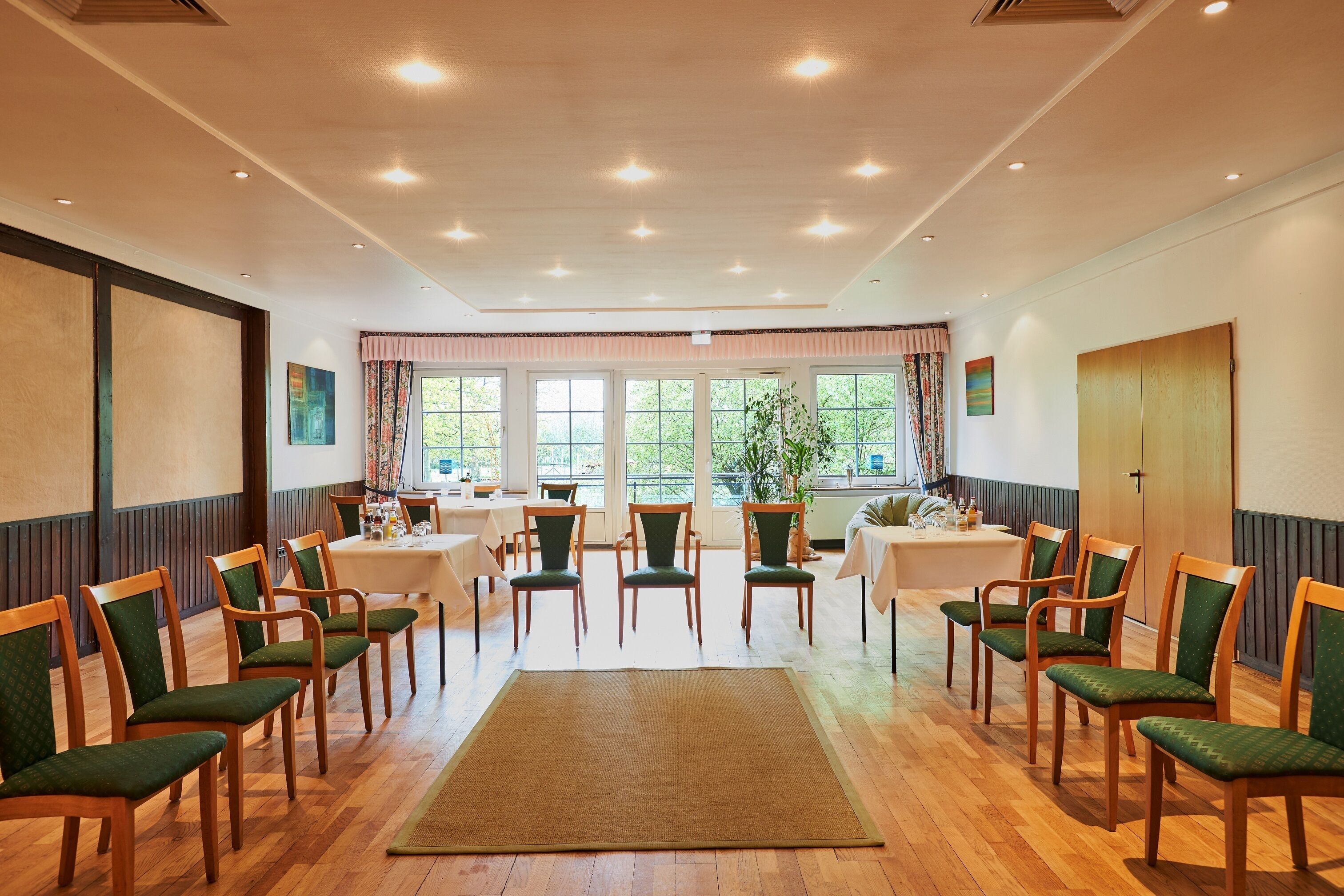 A conference room with wooden chairs, tables, and a large window with curtains.