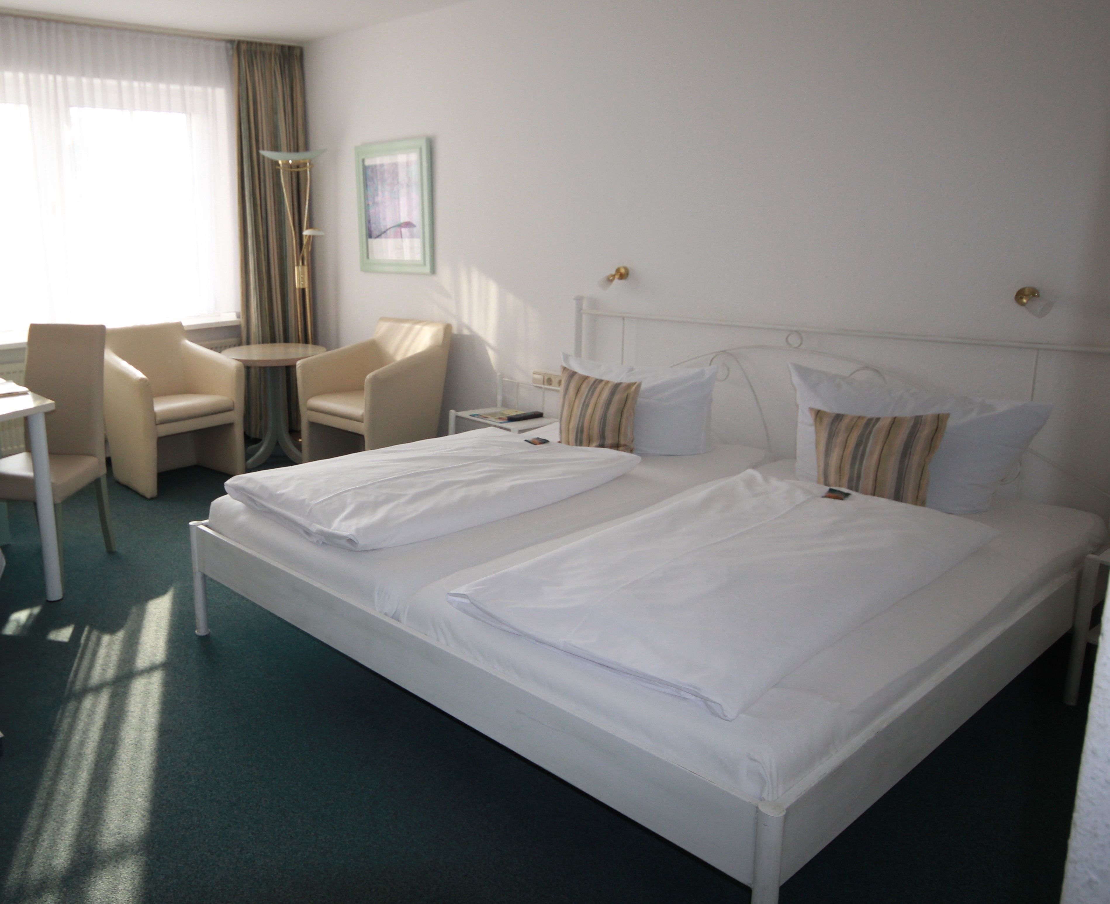 Habitación de hotel con una cama grande, dos mesitas de noche, una silla, una pequeña mesa y una lámpara.