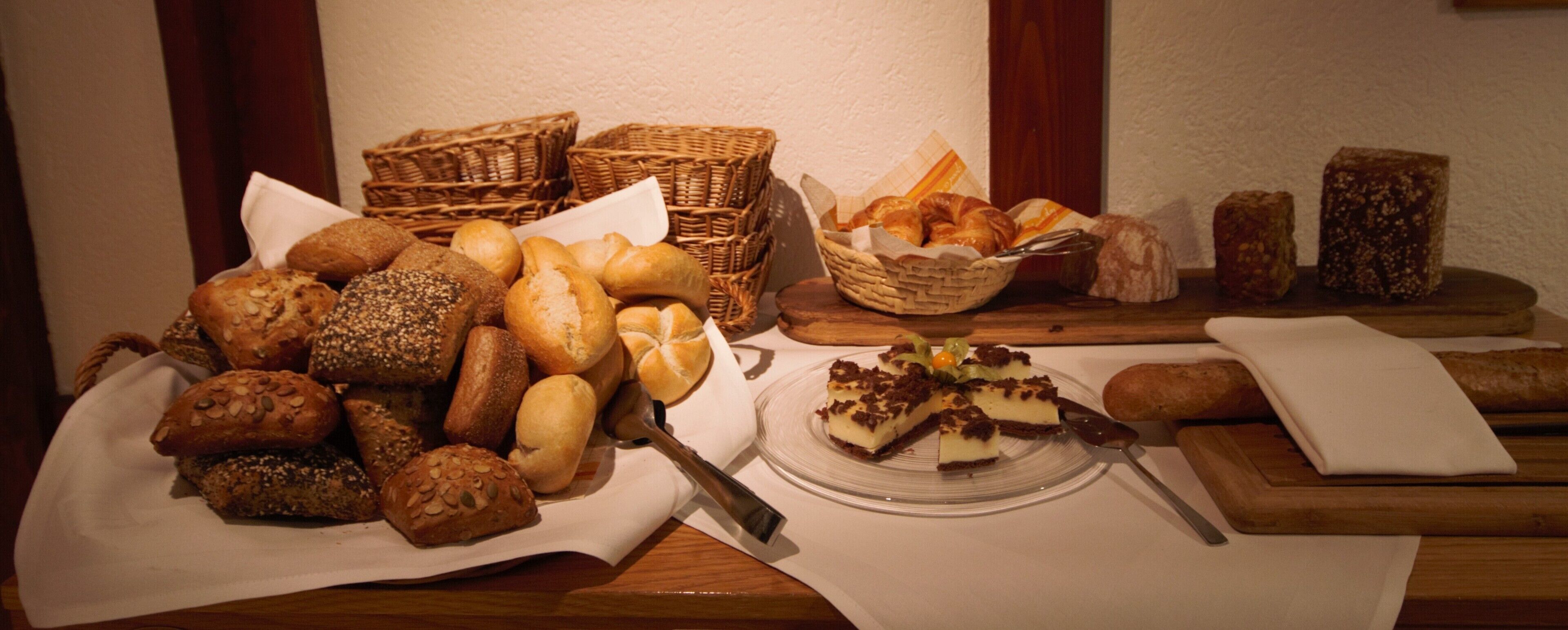 A variety of breads and pastries on a wooden table, with baskets and a plate of dessert.