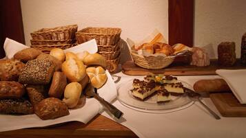 A variety of breads and pastries on a wooden table, with baskets and a plate of dessert.