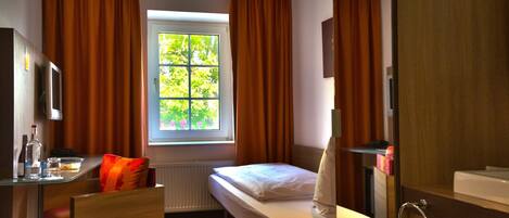 A hotel room with a bed, a desk with a chair, a bathroom with a mirror and sink, and a window with curtains.