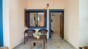 A hallway with patterned floor tiles, two wicker chairs, a small table with a flower vase, and a door leading to another room. - Mistral Holidays (Benaulim)