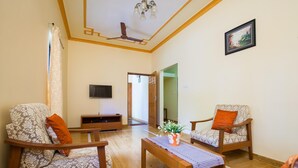 A living room with two patterned armchairs, a wooden coffee table, a flat-screen TV, and a framed picture on the wall. - Mistral Holidays (Benaulim)