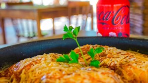 Un plat composé de viande effilochée et de fromage, garni de persil, avec une canette de Coca-Cola rouge en arrière-plan.