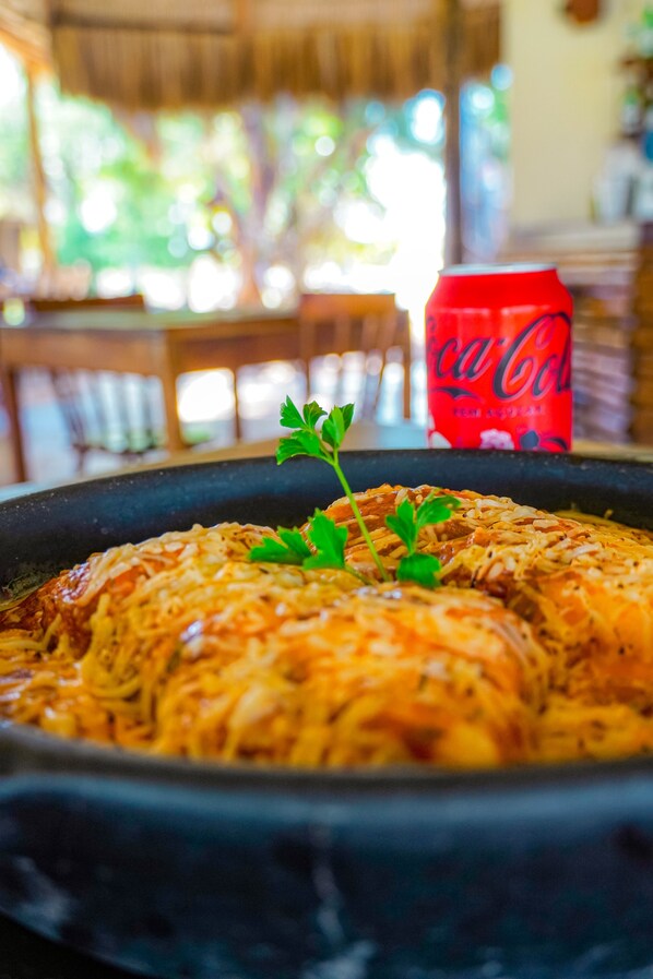 A dish with shredded meat and cheese garnished with parsley, with a red Coca-Cola can in the background. - Hotel Casa do Mar (Icapuí)