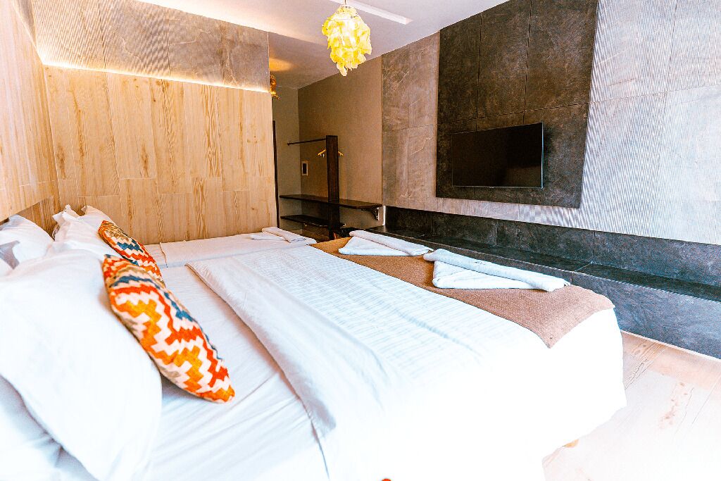 A modern hotel room with a large bed, a TV mounted on the wall, and a wooden accent wall.