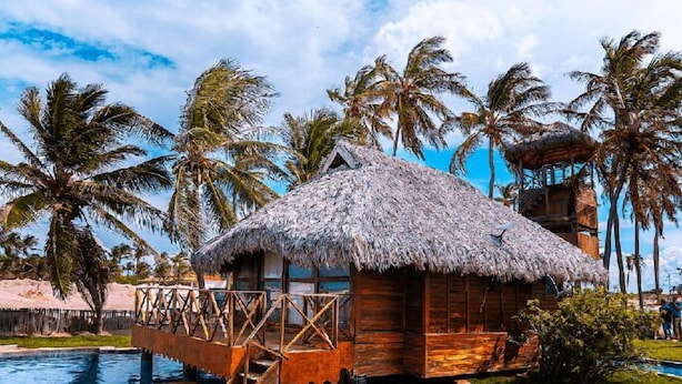 Un espace piscine doté d’une structure en bois et d’un toit de chaume, entouré de palmiers.