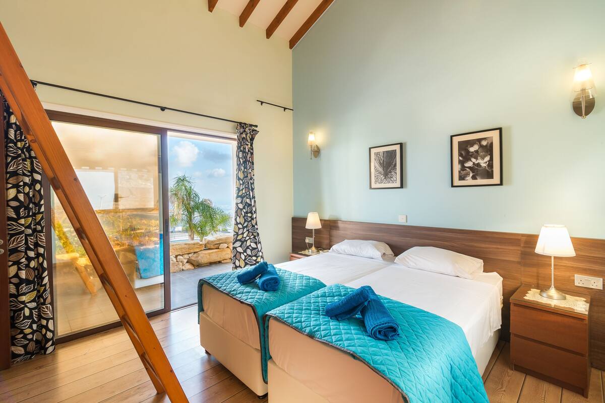 A hotel room with two beds, a balcony, and a view of the outdoors.