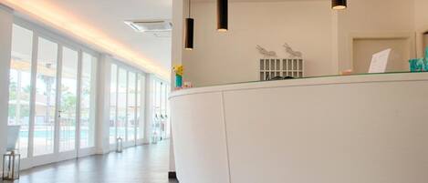 A modern hotel reception area with a curved reception desk, pendant lighting, and large windows offering views of the outdoor area.
