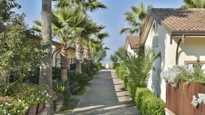 A pathway flanked by palm trees and flowering plants leading to a building with a tiled roof. - Paestum Inn Beach Resort (Capaccio-Paestum)