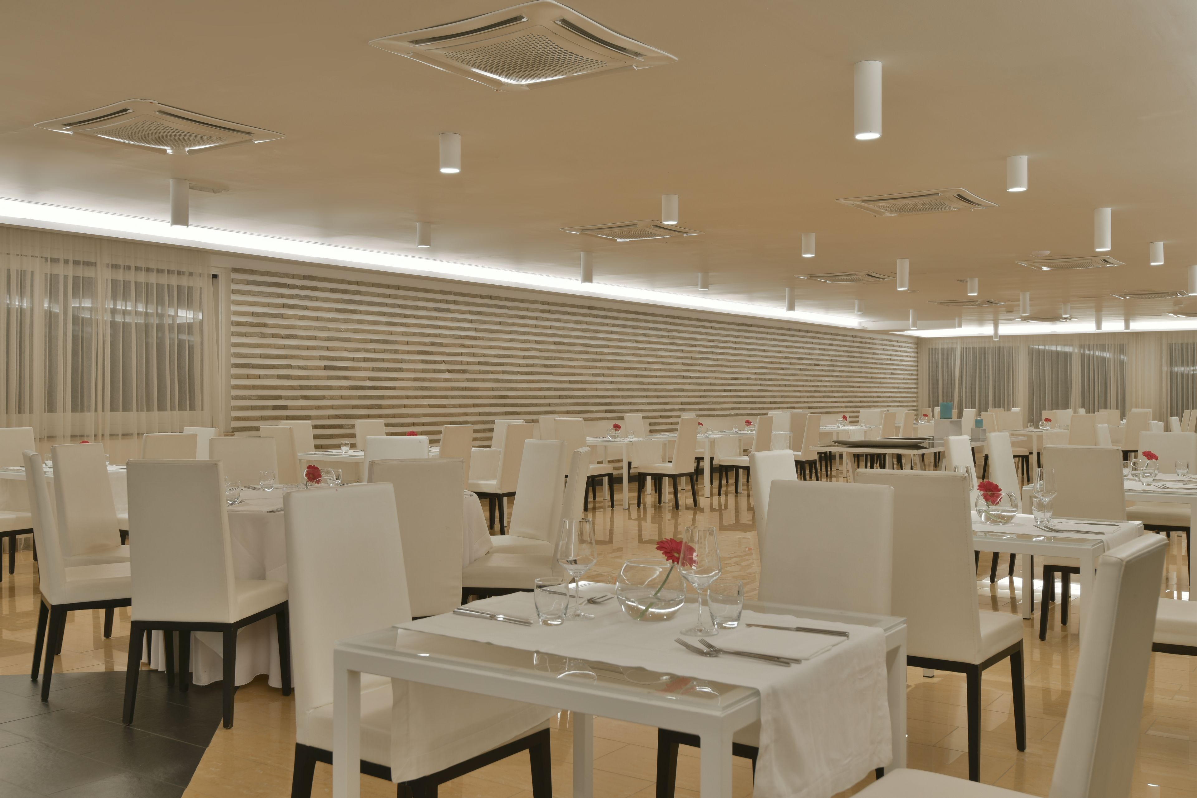 A spacious dining area with multiple tables and chairs, ceiling lights, and a modern design.