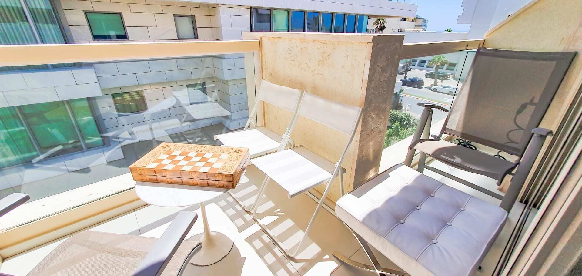 Un balcón con una zona de estar acolchada, una pequeña mesa con un tablero de ajedrez y vistas a la ciudad.
