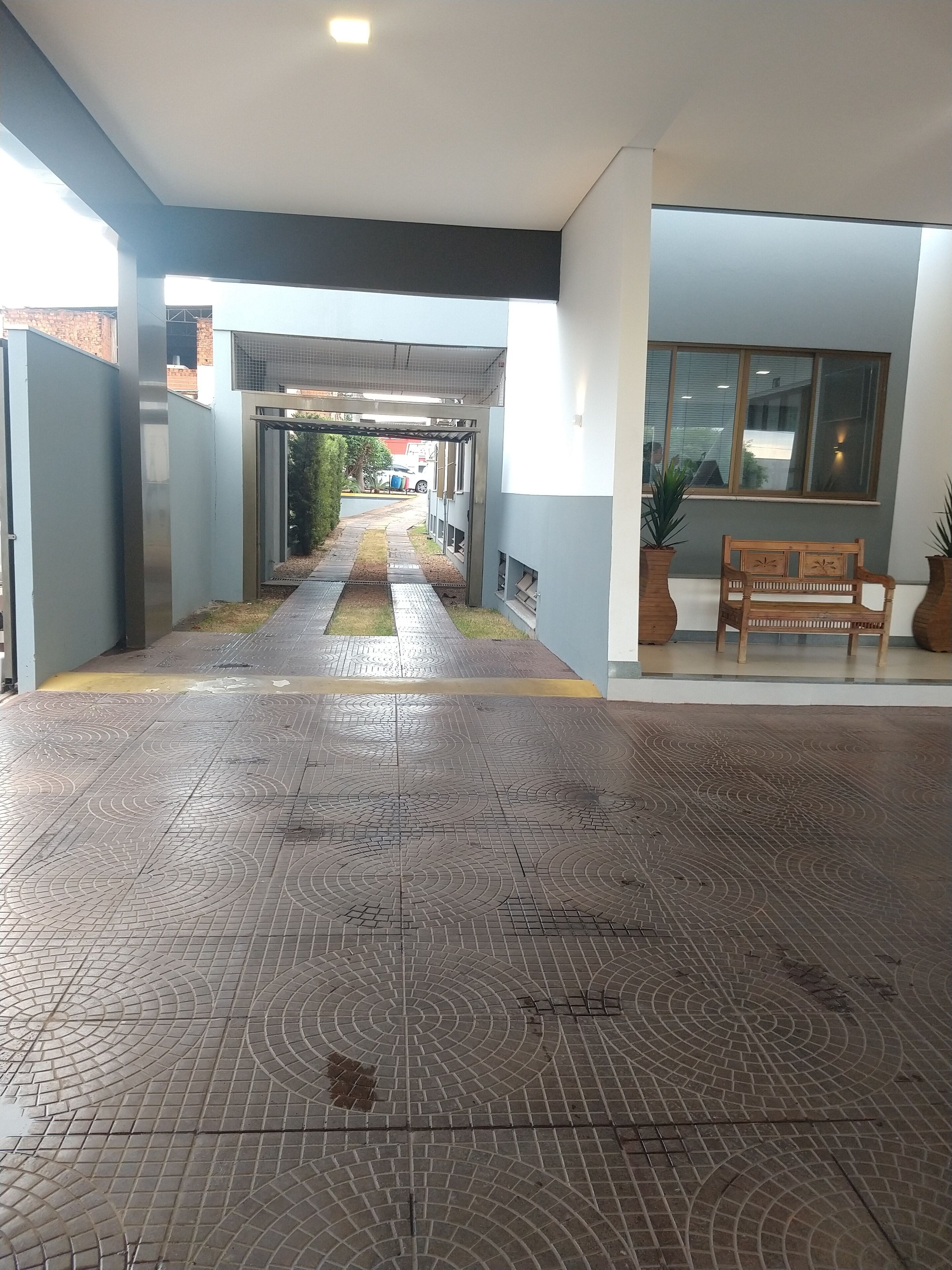 Um espaço amplo e interno com piso estampado, um banco e uma janela com vista para a rua.