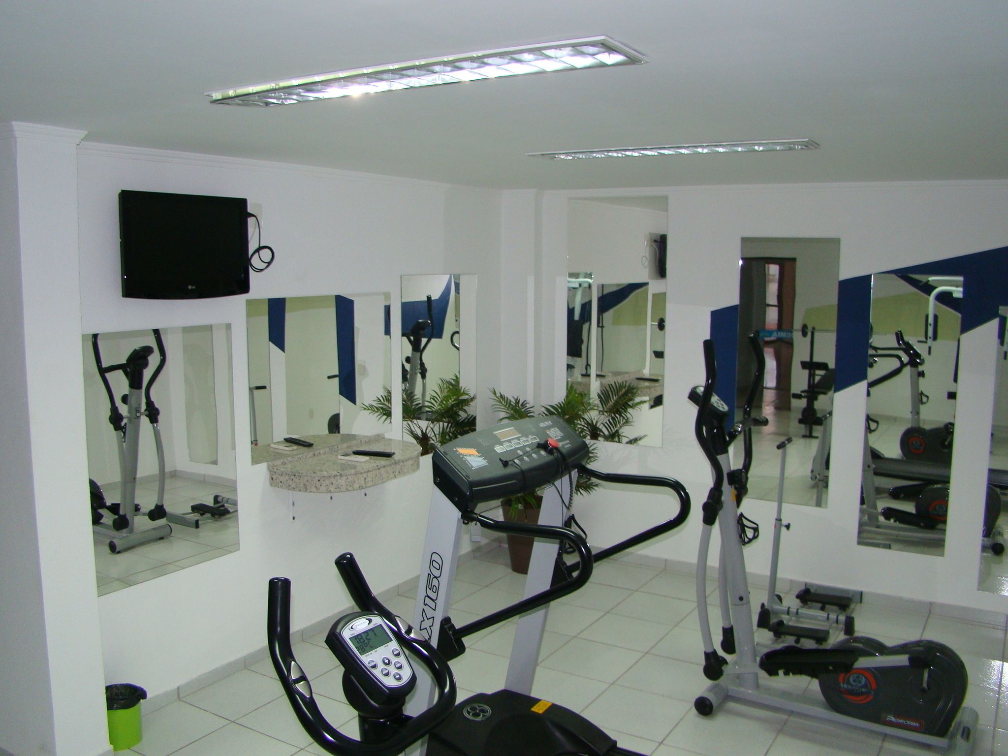 Uma academia com equipamentos de ginástica, espelhos e uma televisão na parede.