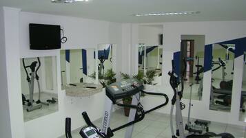 Uma academia com equipamentos de ginástica, espelhos e uma televisão na parede.