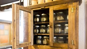 Een houten kast met glazen deuren, gevuld met verschillende potjes voorzien van labels zoals 'Kaneel' en 'Kaneel'.