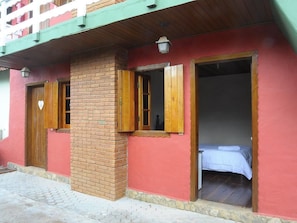 Um edifício com fachada vermelha, persianas de madeira nas janelas e uma cama visível em um dos quartos.