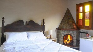 Een slaapkamer met een stenen open haard, een bed met witte lakens en een houten plafond.