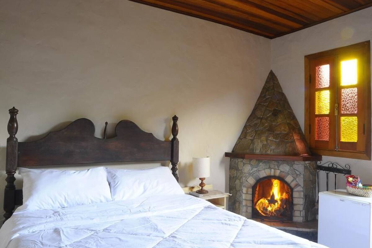 Un dormitorio con chimenea de piedra, cama con ropa de cama blanca y techo de madera.