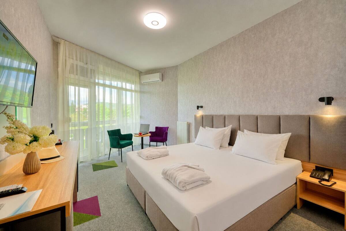 A hotel room with a large bed, a desk with a chair, a TV, and a window with curtains.