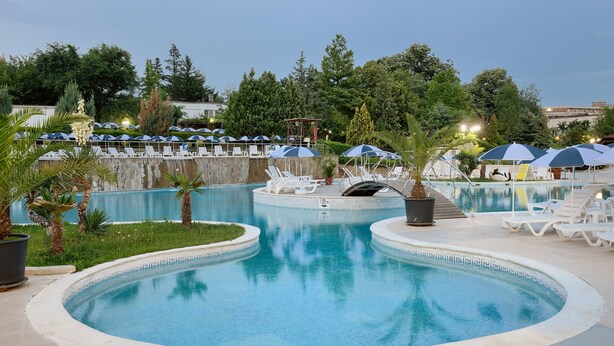 A swimming pool with lounge chairs and umbrellas, surrounded by greenery and trees. - Augusta SPA hotel (Hisarja)
