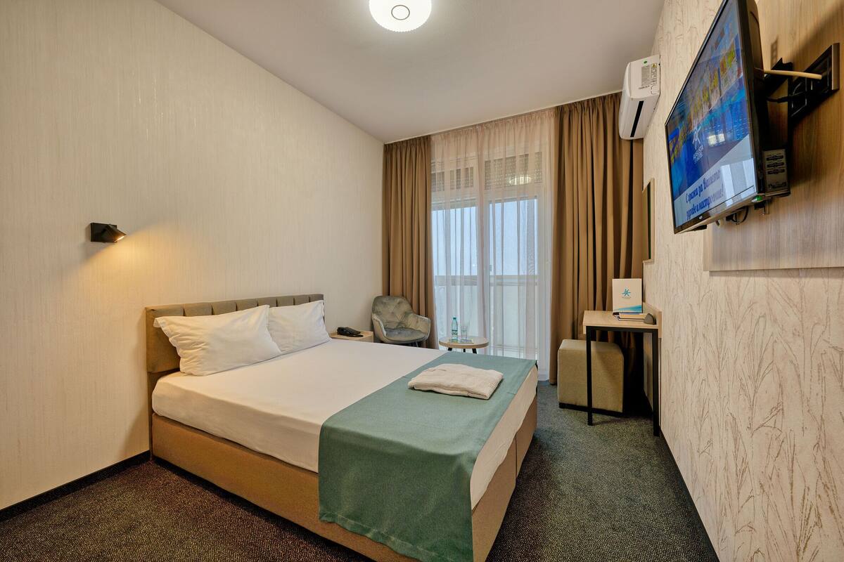 A hotel room with a bed, a desk, a chair, and a television on the wall.
