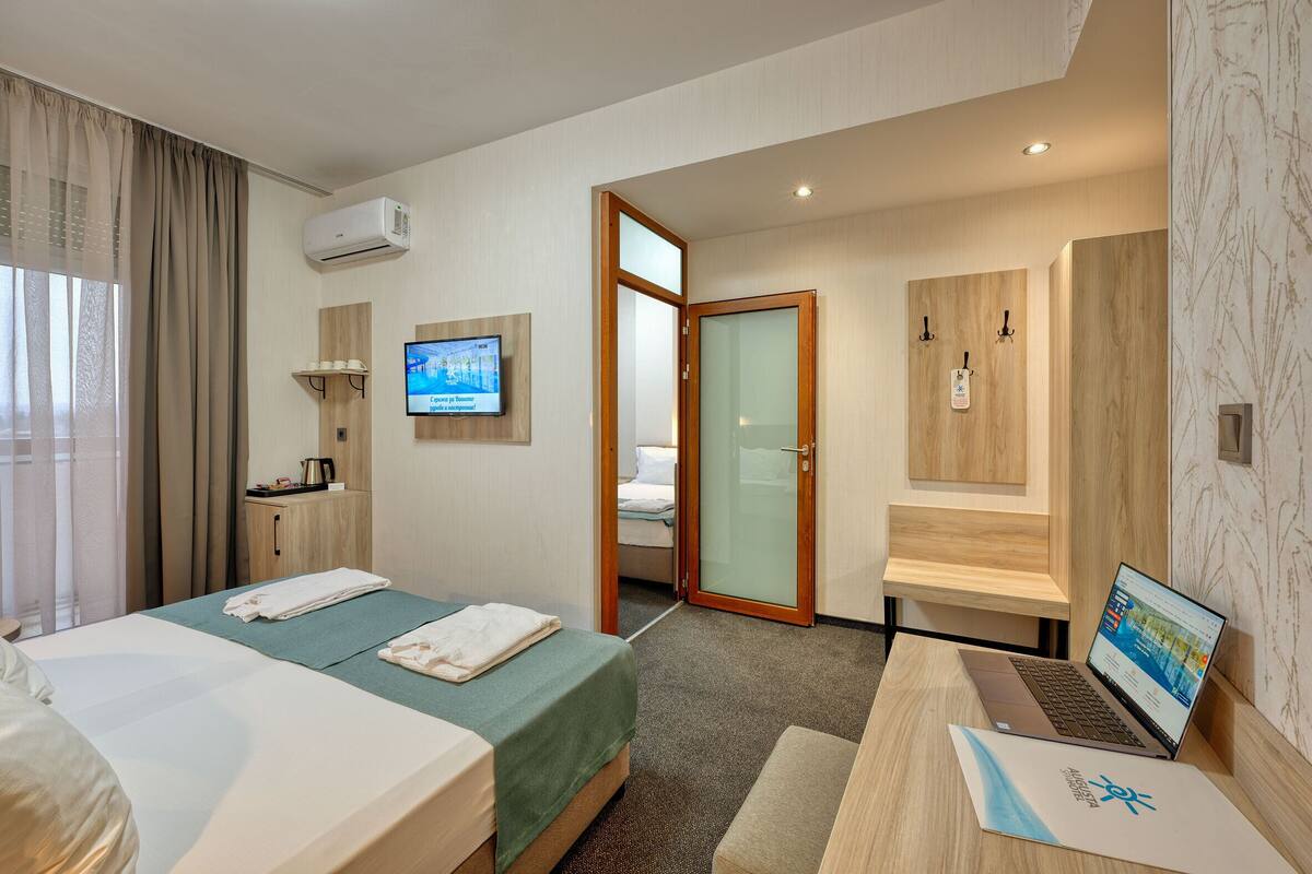A hotel room with two beds, a desk with a laptop, a TV, and a bathroom visible through an open door.