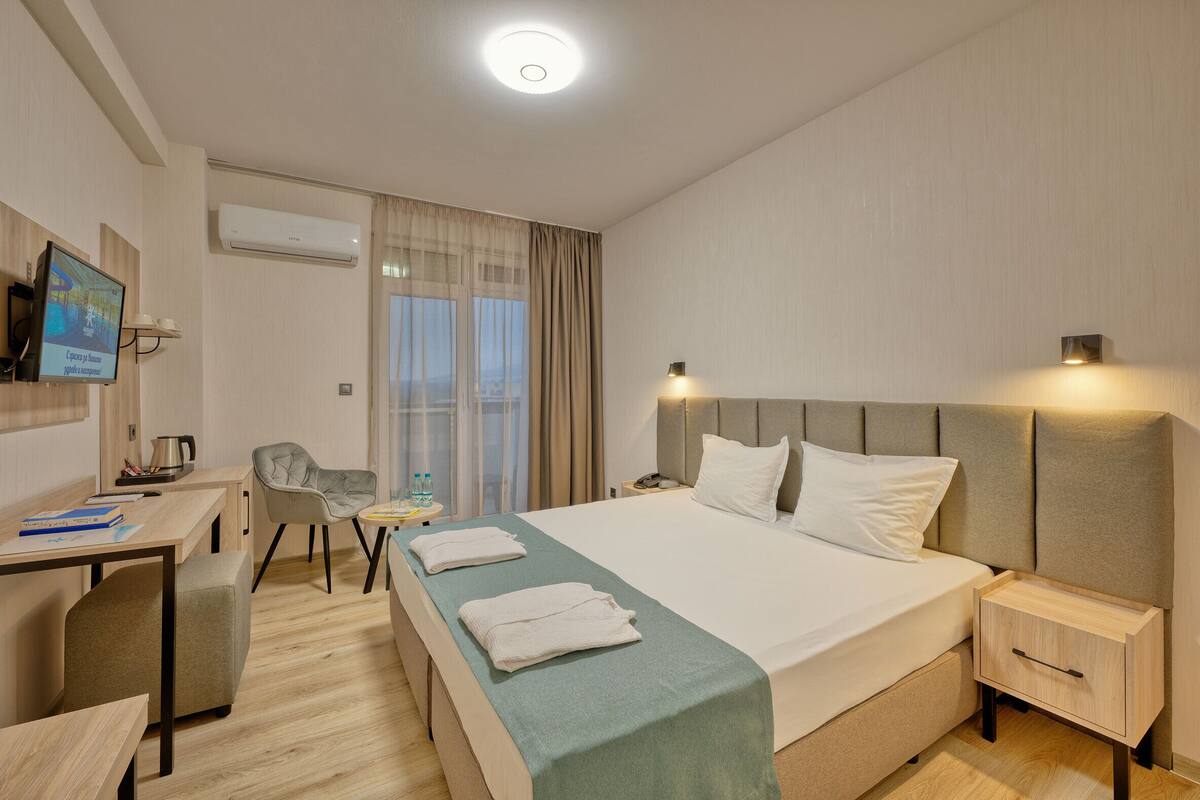 A hotel room with a bed, bedside tables, a desk, a chair, and a television.