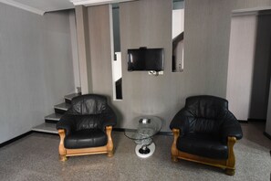 A modern living room with two leather armchairs, a glass coffee table, and a flat-screen TV mounted on the wall. - New House in Old Tbilisi  (Tbilisi)