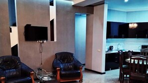 Un salon moderne avec deux fauteuils en cuir, un téléviseur fixé au mur et un lustre.