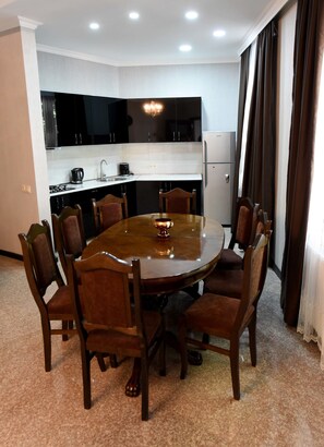 A dining area with a round table and eight chairs, a kitchen with black cabinets and a white countertop, and a refrigerator.