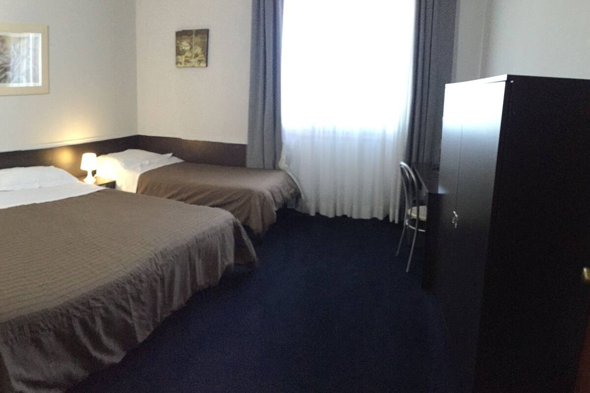 A hotel room with two beds, a desk, a chair, and a TV.