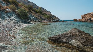 Una costa rocosa con agua cristalina, una colina con vegetación escasa y una vista distante del mar.