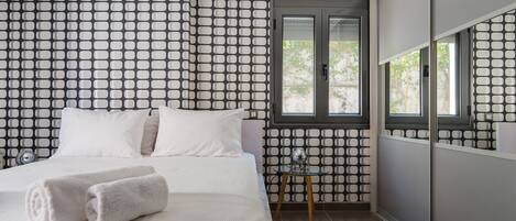 A bedroom with a bed, two pillows, a bedside table with a lamp, and a window with a view of trees.