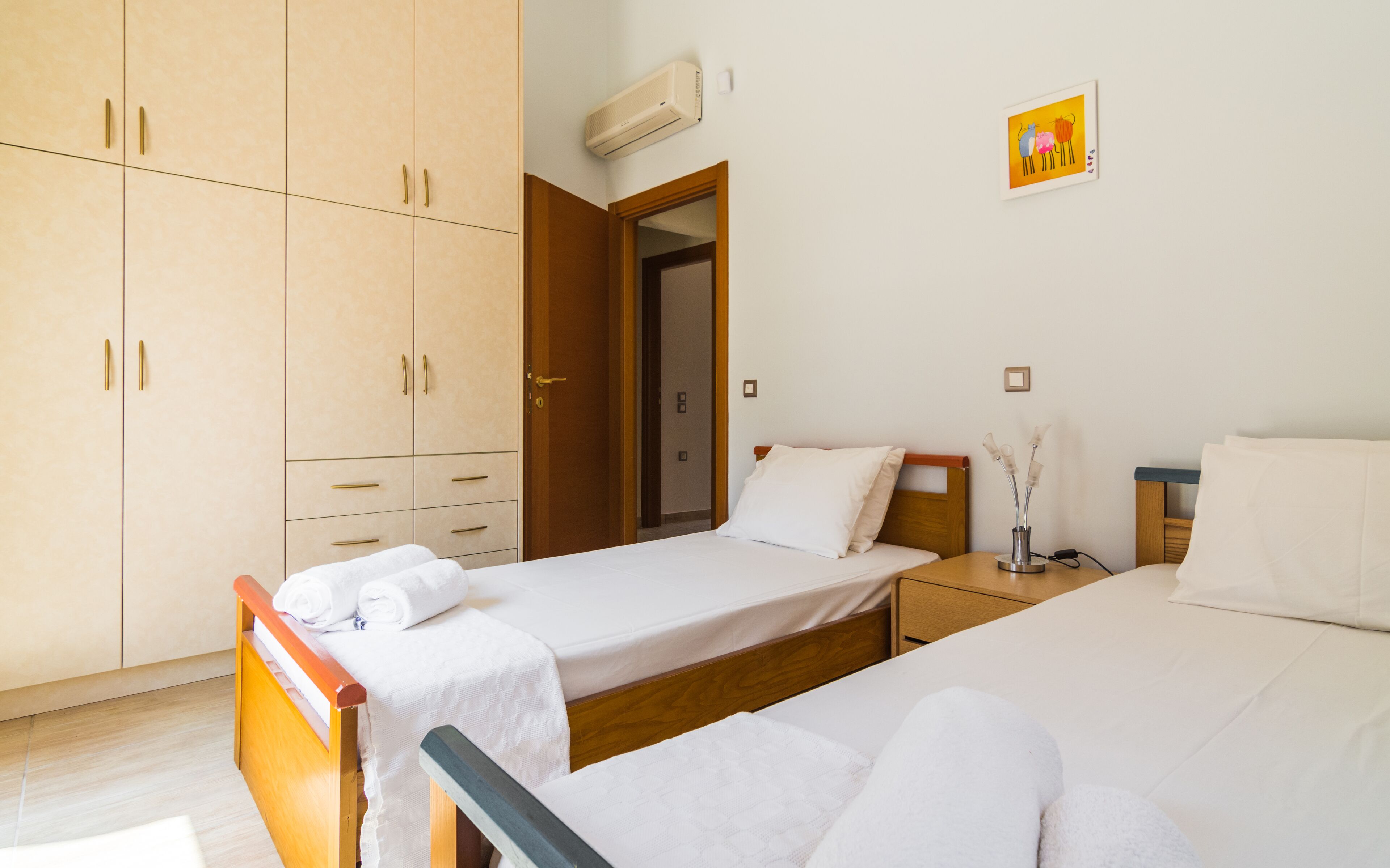 Habitación de hotel con dos camas individuales, un armario, un equipo de aire acondicionado y un cuadro pequeño en la pared.