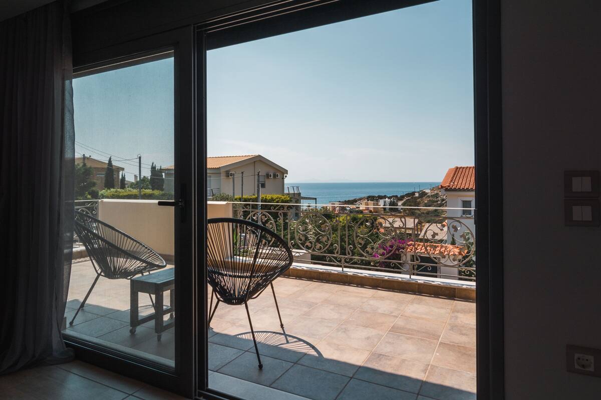 Un balcón con dos sillas, una mesa y vistas al mar y edificios.